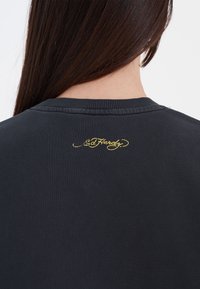 Czarna bluza z ribbowanym dekoltem i teksturowanym materiałem. Złoty haftowany logo "Ed Hardy" umieszczone na tylnym dekolcie.