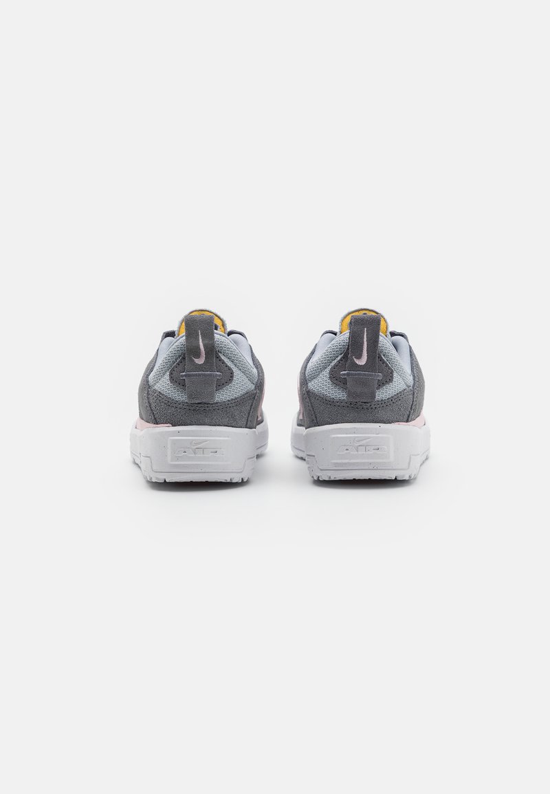 Chaussures de sport grises avec une tige texturée, semelles blanches, accents jaunes et une languette à l'arrière, présentant un logo visible sur le talon.