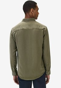 Vihreä pitkähihaisten nappipaitojen olivinvihreä väri, sileä pinta, tavallinen kaulus ja säädettävät hihansuut. Takana on kaareva sauma.