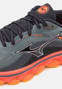 Scarpa da corsa con tomaia in mesh grigio, dettagli neri, suola arancione, particolari riflettenti e un logo nero ben visibile sul lato.