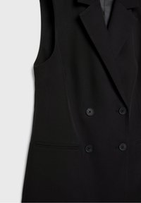 Gilet noir à double boutonnage avec un design structuré, présentant deux poches avant et deux boutons noirs. Texture lisse et coupe ajustée.