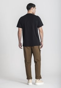 Černé tričko s krátkým rukávem, volný střih, v kombinaci s khaki kalhotami, s ohrnutými manžetami a světlými teniskami. Jednoduchý, neformální outfit bez vzorů.