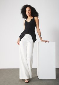 Top negro sin mangas con bordes de encaje, cuerpo ajustado y dobladillo acampanado. Complementado con pantalones anchos blancos y sandalias negras con tiras.