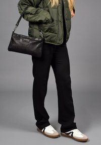 Bolso de cuero negro, chaqueta de plumas verde, pantalones negros y zapatillas blancas con acentos beige. Materiales texturizados, diseño casual.