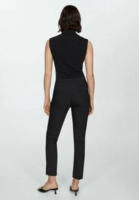 Top nero senza maniche con colletto alto abbinato a pantaloni neri slim-fit con vita media e spacchi laterali, indossati con sandali con tacco neri.