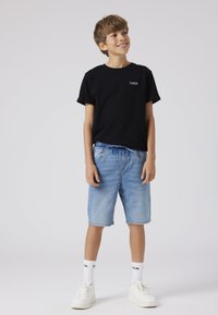 Svart bomulls-T-shirt med tryck, kombinerad med ljusblå denimshorts. Vita sneakers och mönstrade strumpor kompletterar outfiten.