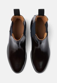 Botas de piel negras hasta el tobillo con paneles laterales elásticos, textura suave y diseño de punta redondeada. Cuenta con un forro interior marrón y una tira para tirar.