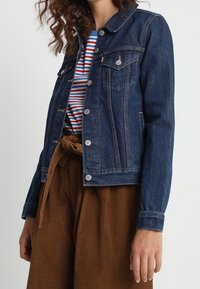 Dark blue denim jacket with a classic collar, button front, and chest pockets. Paired with a striped shirt and brown corduroy pants.
