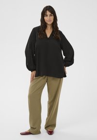 Blusa nera leggera a maniche lunghe con scollo a V, abbinata a pantaloni larghi color sabbia e ballerine bordeaux. Design semplice e pulito con una texture morbida.