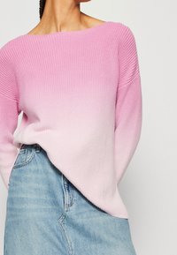 Lichtroze gebreide trui met een off-the-shoulder ontwerp en ribbeltextuur, gecombineerd met een lichtblauwe denimrok.