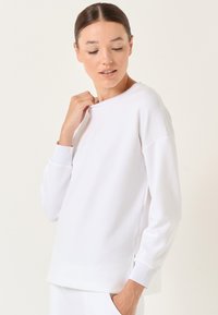 Felpa bianca con colletto a girocollo, vestibilità rilassata, polsini a costine e texture liscia. Presenta spalle scese per un maggiore comfort.
