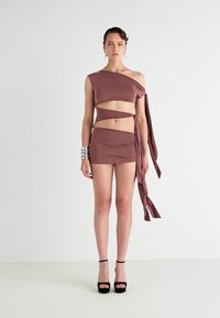 Hnedý dvojdielny outfit pozostávajúci z topu na jedno rameno a mini sukne, vyrobený z mäkkého materiálu s prekrytými popruhmi a viazaním.