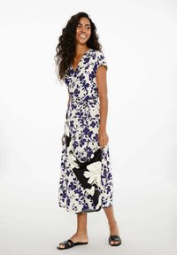 Kvetinové šaty s viazaním v bielej farbe s námorníckymi modrými a čiernymi akcentmi. Majú krátke rukávy, zúžený pás a dlhú sukňu s živým dizajnom.