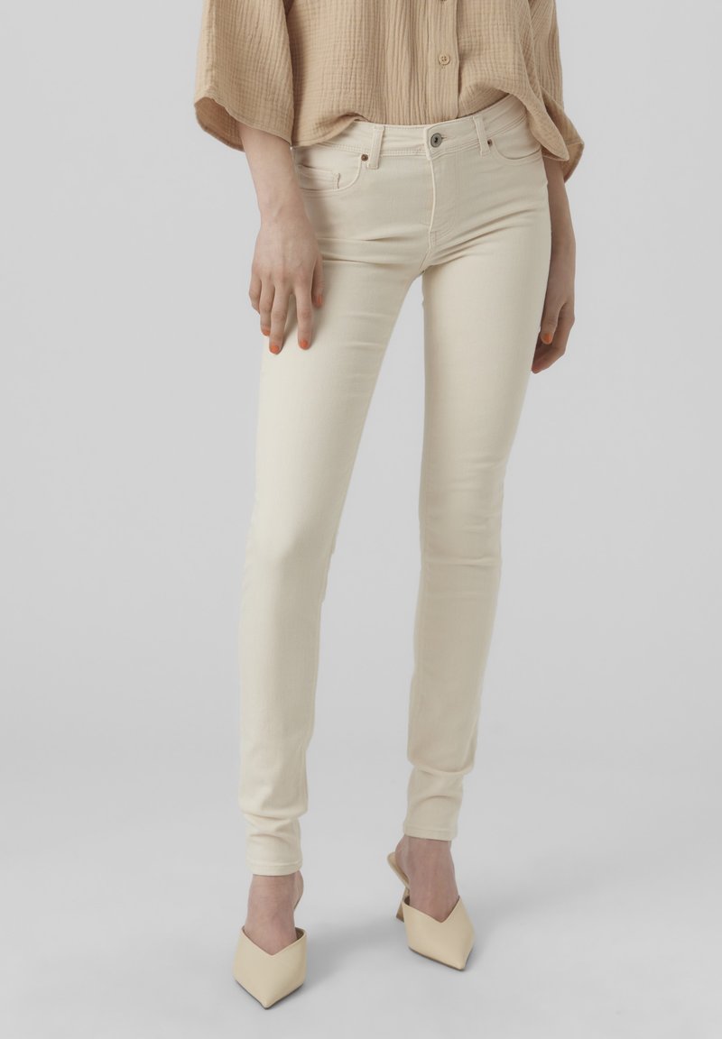 Krémově bílé skinny džíny z bavlněné směsi, s vysokým pasem a úzkými nohavicemi, spárované s lehkými béžovými muly.