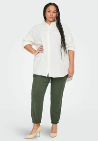 Chemise en lin blanche à boutons avec des manches retroussées, associée à un pantalon cargo vert olive avec des poignets élastiques, et des escarpins beiges à bout pointu.