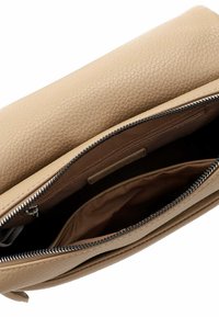 Intérieur d'un sac à main en cuir beige avec un compartiment zippé, mettant en valeur une texture lisse et un doublage en tissu doux à l'intérieur.