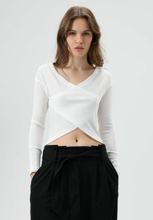 Witte geribbelde top met lange mouwen, V-hals en overslagontwerp, gecombineerd met zwarte, hooggetailleerde broek met ceintuur.