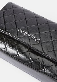 Čierna prešívaná kožená peňaženka s lesklým povrchom, s jemným strieborným logom "VALENTINO", diagonálnym šitím a elegantným obdĺžnikovým tvarom.