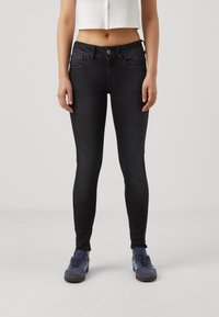 Black skinny jeans with a smooth texture, high waist, front pockets, and button closure, paired with dark blue sneakers featuring light blue accents.