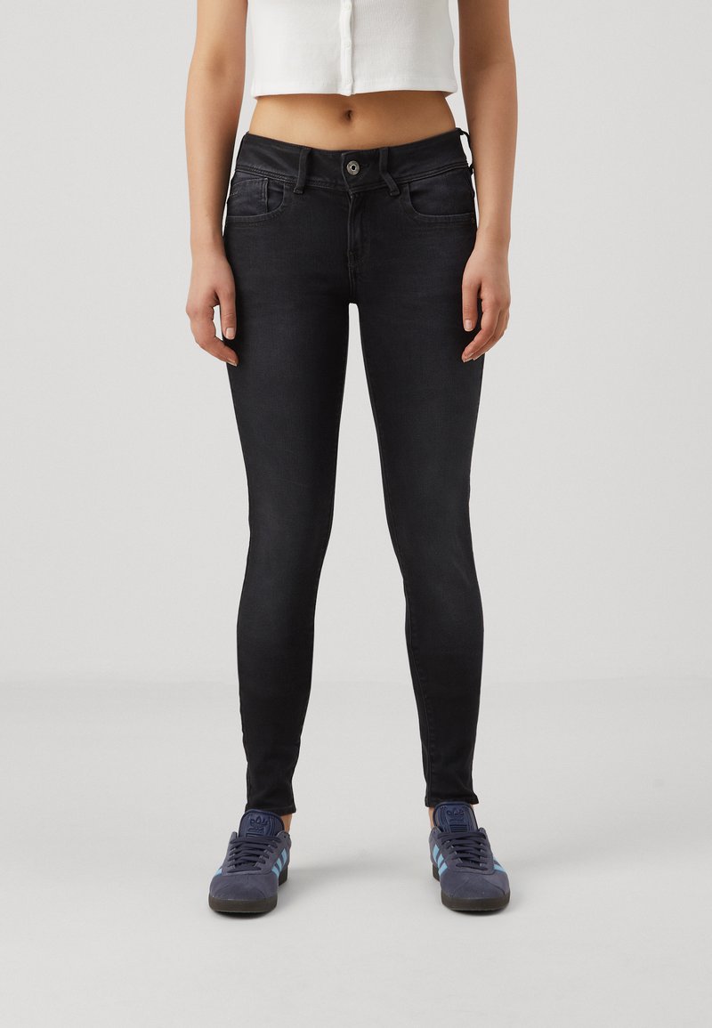 Svarta skinny jeans med en slät textur, hög midja, framfickor och knappstängning, ihop med mörkblå sneakers med ljusblå detaljer.