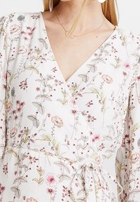 White floral wrap dress featuring pink and green patterns, v-neckline, long sleeves, and a tie at the waist. Lightweight fabric.