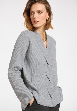 Suéter gris de canalé con un profundo escote en forma de V y un detalle de frente retorcido. Cuenta con mangas largas y un ajuste relajado. Material de punto suave y texturizado.