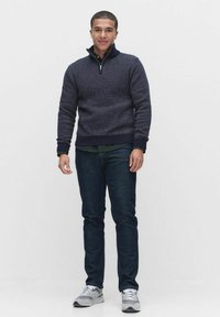 Mörkblå zip-neck tröja med ett strukturerat mönster, kombinerad med mörka denimjeans och ljusgråa träningsskor.