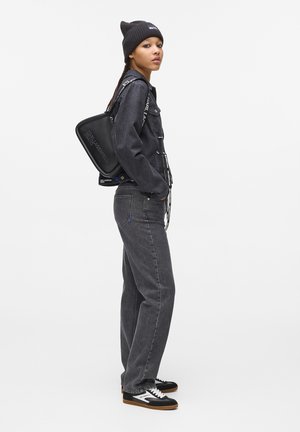 Veste en denim noire et pantalons avec une finition texturée, associés à un sac noir élégant et des sneakers noires avec des accents blancs.