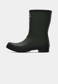Botte de cheville en caoutchouc verte avec une finition texturée, un talon bas et une bordure noire en haut. Présente un patch logo sur le côté.