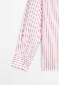 Poignet de chemise à manches longues avec des rayures verticales blanches et roses, avec un bouton blanc et une couture rose sur le poignet et la manche.