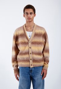 Mjuk randig cardigan i bruna och gula nyanser, tillverkad av fluffigt material, med en djup V-ringning, framknäppning och ribbade muddarbågar.