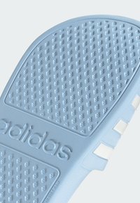 Light blue Adidas shoe sole with textured surface, featuring raised patterns for grip. Includes embossed logo and white accent stripes.