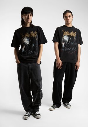 Des t-shirts graphiques noirs présentent un design à l'avant avec des chevaliers. Associé à un pantalon noir ample et des chaussures de style converse, le look général est décontracté.