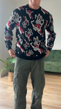 Schwarzer Pullover mit grafischen Schädeln und Händen in Weiß, Rot und Beige. Kombiniert mit olivgrünen Cargo-Hosen mit Seitentaschen.