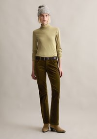 Khaki golf, oliwkowe spodnie z kordurowej tkaniny o subtelnej fakturze, ciemnobrązowy pasek oraz szary dzianinowy beanie. Beżowe botki na obcasie dopełniają całość.