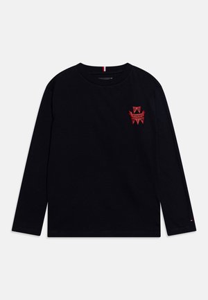 Czarna koszulka z długim rękawem i okrągłym dekoltem, z małym czerwonym emblematem z napisem "Go Tommy Win" na lewej piersi oraz niewielkim logo na lewym mankiecie.