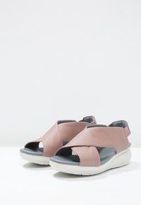 Sandali in pelle rosa con design a punta aperta, dettagli a fascia incrociata e una soletta grigia imbottita su una suola in gomma bianca.