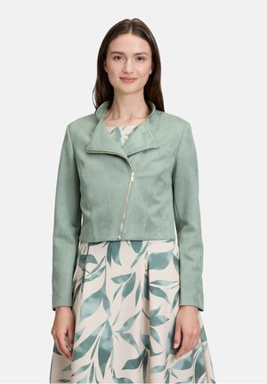 Mintgroene faux-suède cropped jack met een geknipt kraag en asymmetrische rits, gecombineerd met een bloemenpatroon jurkje.
