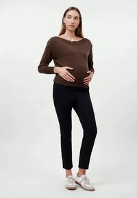 Suéter marrón de punto con canalé y escote amplio, usado sobre un pantalón negro ajustado. La modelo lleva zapatillas blancas, con las manos apoyadas en su barriga.