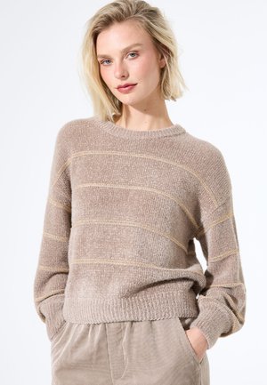 Pull en beige texturé avec des rayures dorées, encolure ronde et épaules tombantes. Fil doux et détails de bord-côte. Associé à un pantalon clair.