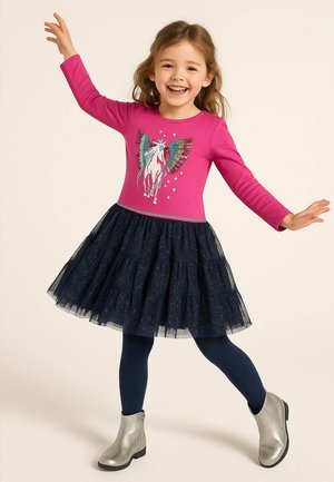 Rosa Langarmkleid mit einem Einhorn-Graphic, gestuftem marineblauen Tüllrock und silbernen Ankle Boots. Dunkelblaue Strumpfhosen runden das Outfit ab.