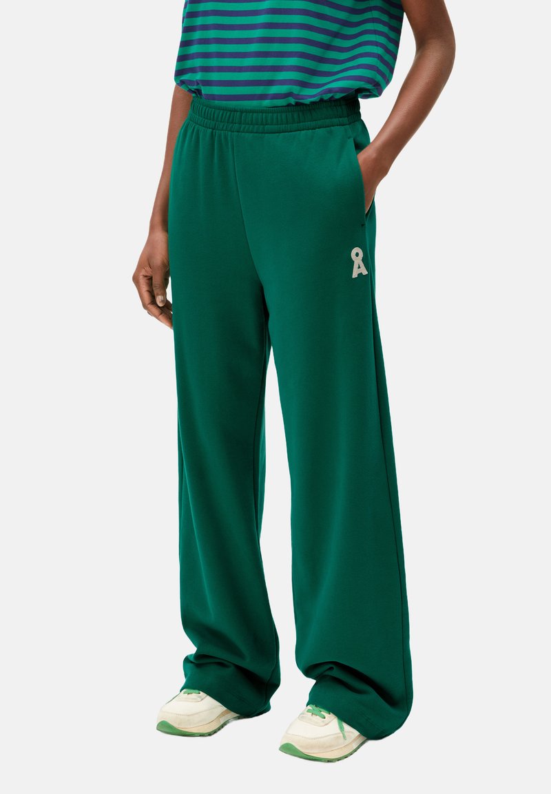Pantalons de survêtement larges verts en tissu doux, avec une taille élastique et un petit logo brodé sur le côté gauche.