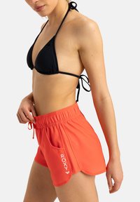 Roxy korallfärgade simshorts med elastisk midja, dragsko och en sidoficka med logotyp. Svart bikinitetopp fulländar looken.