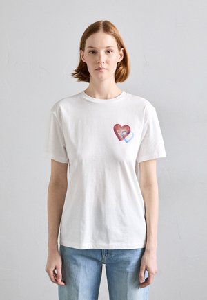 T-shirt in cotone bianco con design a cuore rosso e accenti blu sul lato sinistro del petto, collo rotondo standard e maniche corte.