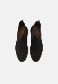 Svart mocka slip-on skor med elastiska sidopaneler och en vågig brogue-detalj längs tån. Slät innersula och gummisula.