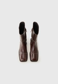 Bottines en cuir marron avec un bout carré et des coutures blanches, dotées de fermetures éclair latérales, présentées sur un fond gris clair.