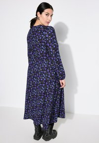Abito lungo e fluido in tessuto nero con motivi floreali viola e blu. Presenta maniche lunghe e una vestibilità comoda. Abbinato a stivali militari neri.
