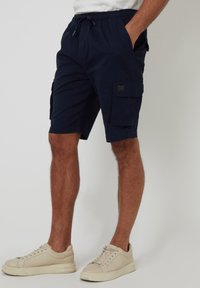 Marineblaue Cargo-Shorts aus Baumwolle, mit elastischem Taillenbund, Seitentaschen und einer aufgesetzten Tasche am linken Oberschenkel.
