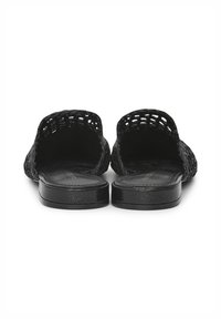 Une paire de mules plates tissées noires à enfiler, avec un dos ouvert et une forme arrondie, vue de l'arrière sur un fond blanc.