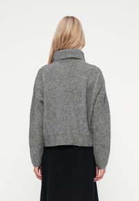 Grå ribbestrikket genser med høy krage og senkede skuldre, cropped lengde, teksturert stoff og åpen ryggdetalj.